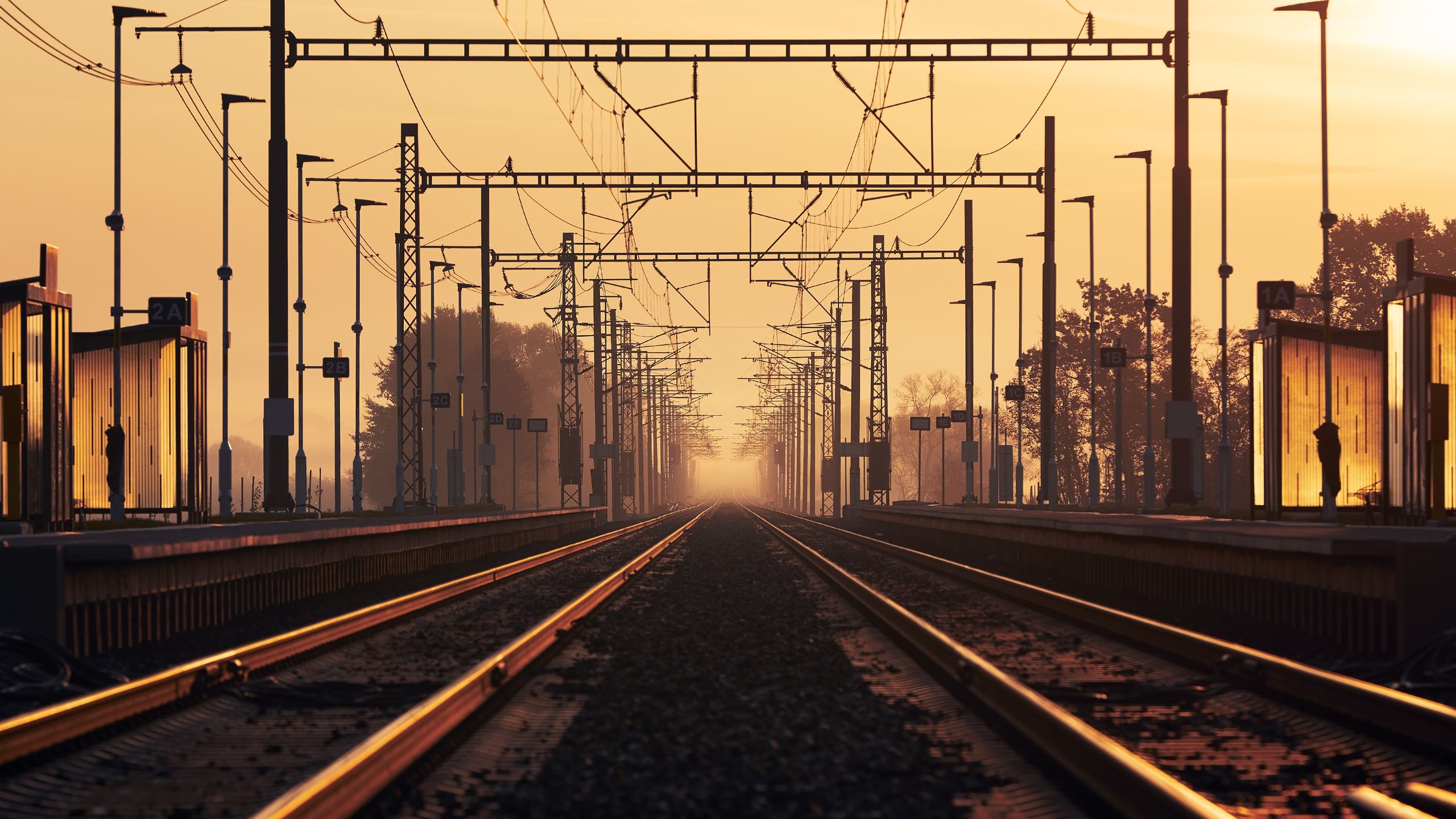 Bahnstrecke mit Oberleitung im Licht des Sonnenaufgangs